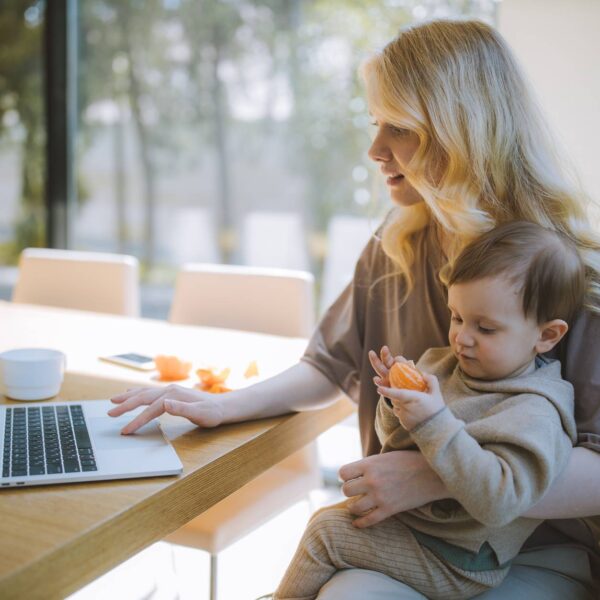 woman carrying her baby and working on a laptop